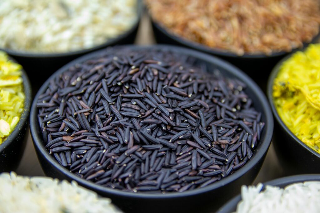 High-quality close-up of black rice in a bowl, with colorful rice varieties surrounding it.